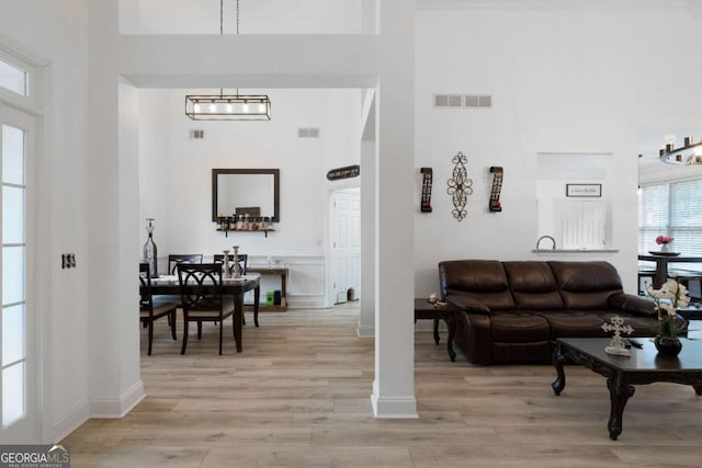 living room with a notable chandelier, light hardwood / wood-style flooring, and a high ceiling