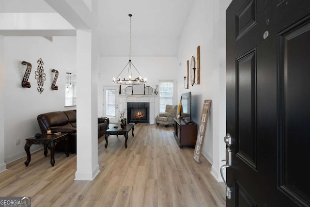 entryway featuring a tiled fireplace, a notable chandelier, high vaulted ceiling, and light hardwood / wood-style flooring