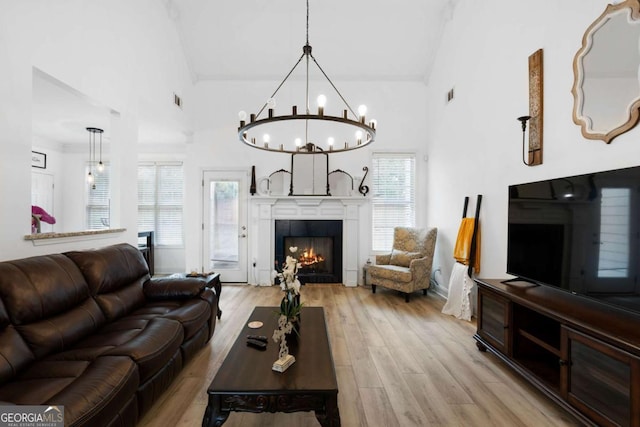 living room featuring high vaulted ceiling, a notable chandelier, a fireplace, and light hardwood / wood-style flooring