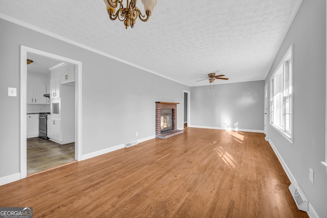 unfurnished living room featuring crown molding, wood-type flooring, ceiling fan with notable chandelier, and a brick fireplace