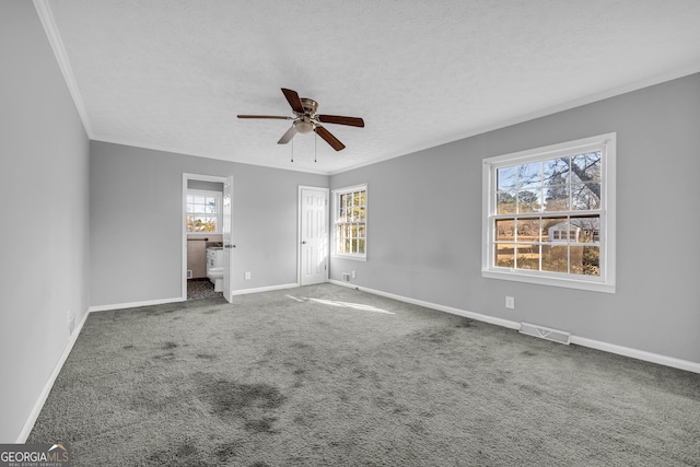 interior space with ceiling fan, dark colored carpet, connected bathroom, ornamental molding, and a textured ceiling