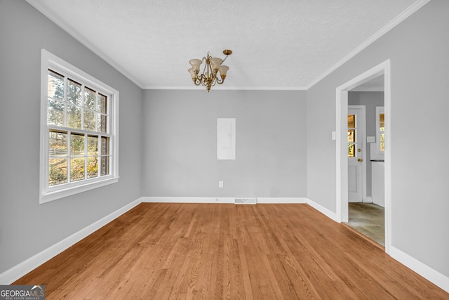 spare room featuring an inviting chandelier, ornamental molding, light hardwood / wood-style floors, and a textured ceiling