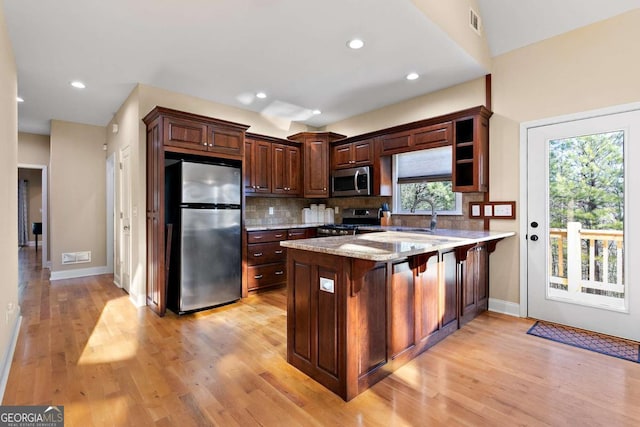 kitchen featuring a breakfast bar, stainless steel appliances, light stone counters, tasteful backsplash, and kitchen peninsula