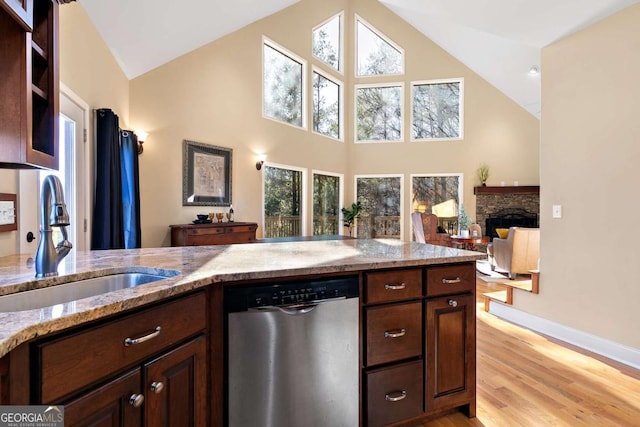 kitchen featuring a fireplace, sink, stainless steel dishwasher, light stone counters, and dark brown cabinets