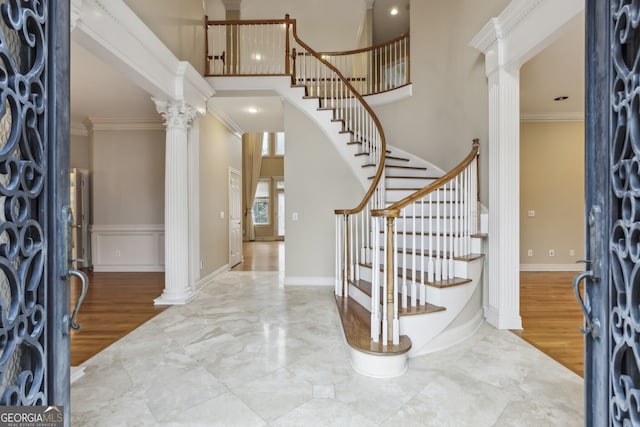 entrance foyer with hardwood / wood-style flooring, a towering ceiling, ornamental molding, and decorative columns