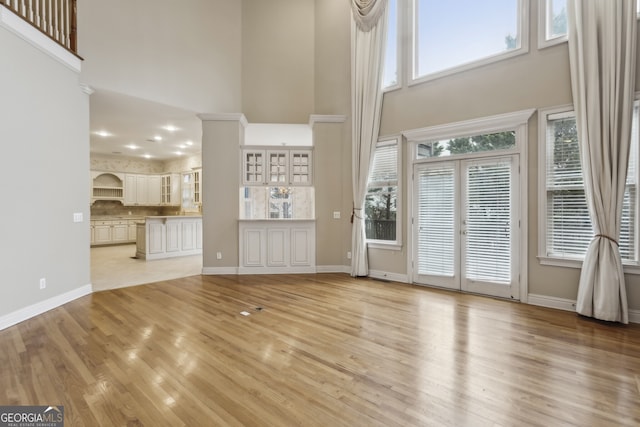 unfurnished living room with light hardwood / wood-style floors, french doors, and a high ceiling