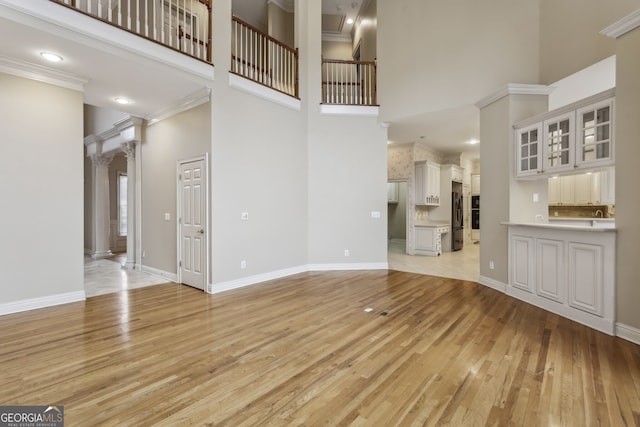 unfurnished living room featuring crown molding, light hardwood / wood-style flooring, and a high ceiling