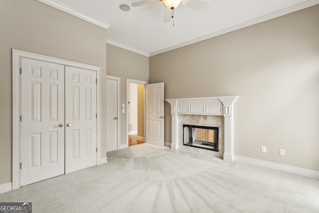 unfurnished living room featuring a premium fireplace, ornamental molding, light colored carpet, and ceiling fan