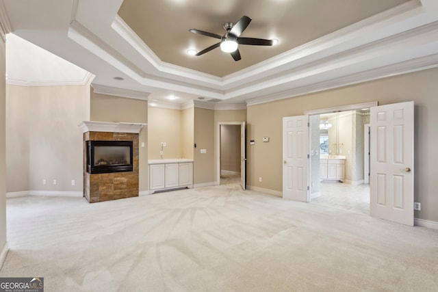 unfurnished living room with light carpet, ornamental molding, a raised ceiling, ceiling fan, and a tiled fireplace