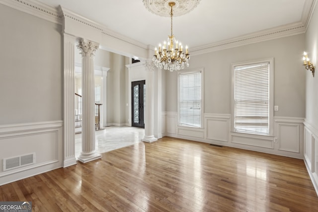 unfurnished dining area with crown molding, a chandelier, decorative columns, and hardwood / wood-style floors