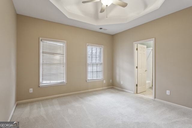 unfurnished bedroom featuring connected bathroom, light colored carpet, and a tray ceiling