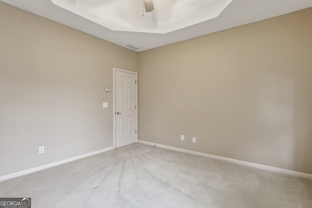 empty room with a tray ceiling, light colored carpet, and ceiling fan