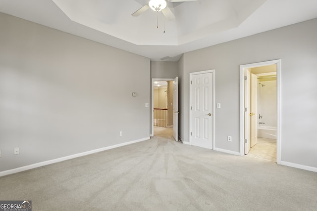 unfurnished bedroom featuring ensuite bathroom, light colored carpet, ceiling fan, and a tray ceiling