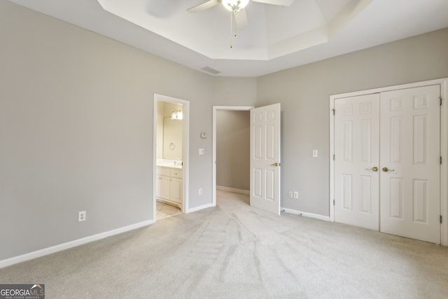 unfurnished bedroom with connected bathroom, light carpet, a raised ceiling, a closet, and ceiling fan