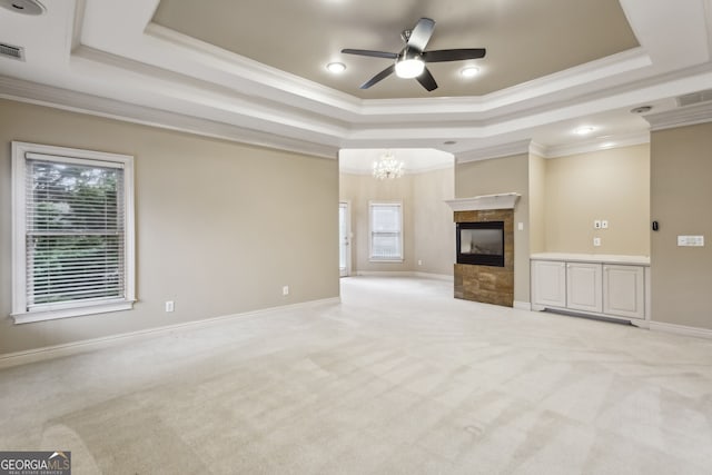 unfurnished living room with ornamental molding, a tray ceiling, a fireplace, and light colored carpet