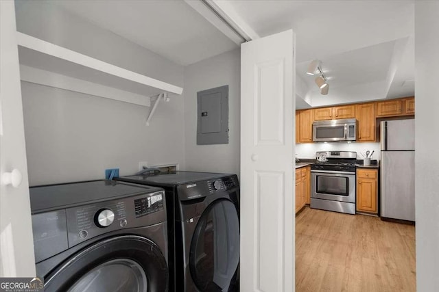 clothes washing area with washing machine and dryer, electric panel, and light hardwood / wood-style floors