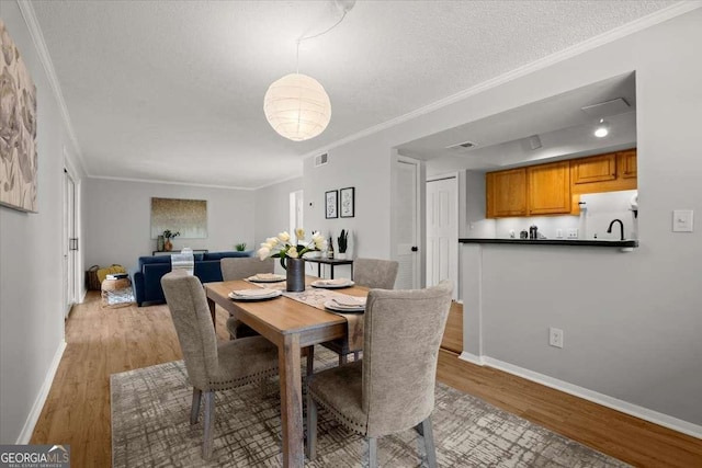 dining space featuring ornamental molding, a textured ceiling, and light hardwood / wood-style floors