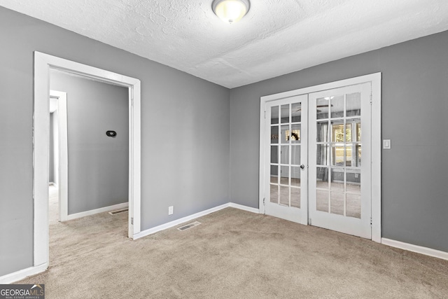 carpeted spare room featuring a textured ceiling and french doors