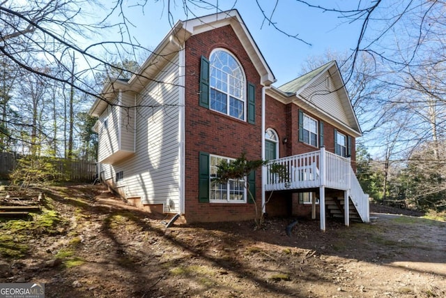 view of property exterior with brick siding, stairway, and fence