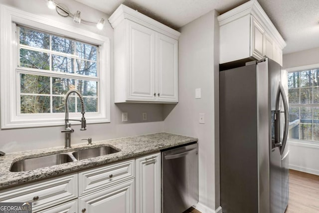 kitchen featuring a sink, stainless steel appliances, light stone counters, and white cabinets