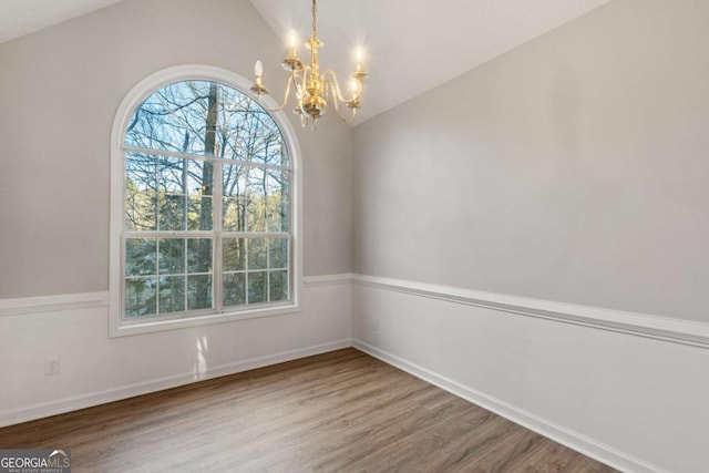 unfurnished dining area featuring a notable chandelier, wood finished floors, and vaulted ceiling