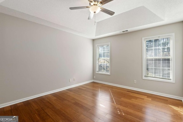 empty room with visible vents, a ceiling fan, hardwood / wood-style floors, baseboards, and a raised ceiling