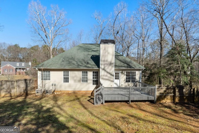 rear view of property with a yard, a wooden deck, a chimney, and fence