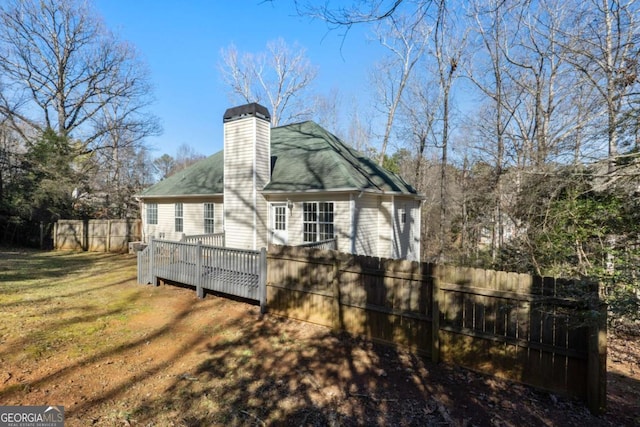 view of side of home with a wooden deck, a lawn, a chimney, and fence