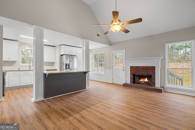 unfurnished living room featuring visible vents, a brick fireplace, ceiling fan, light wood-type flooring, and ornate columns