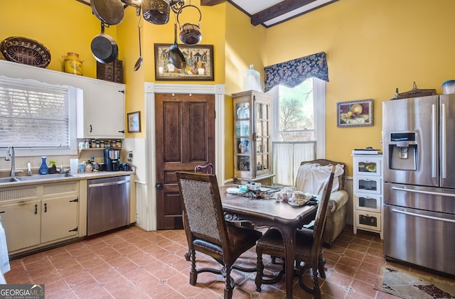 kitchen with sink, appliances with stainless steel finishes, a high ceiling, white cabinets, and beamed ceiling