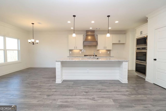 kitchen featuring white cabinets, stainless steel appliances, custom range hood, and an island with sink