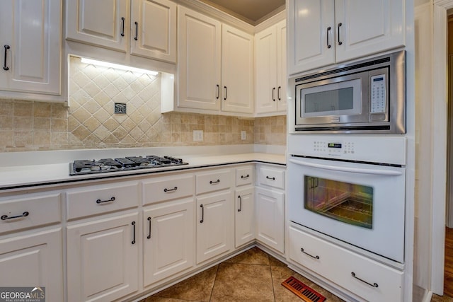 kitchen with tasteful backsplash, appliances with stainless steel finishes, tile patterned flooring, and white cabinets