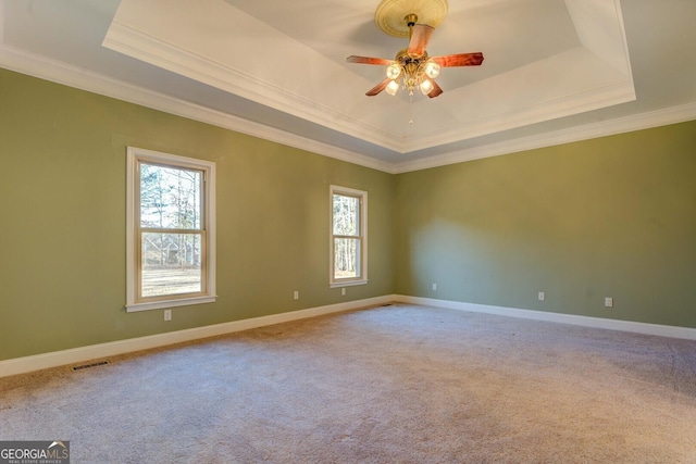 carpeted spare room with a raised ceiling, ornamental molding, plenty of natural light, and ceiling fan