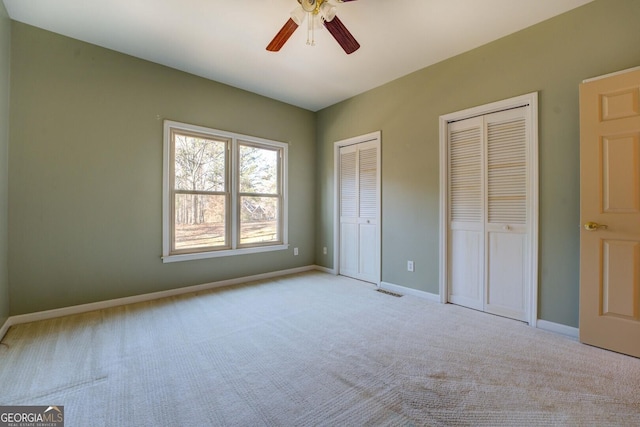 unfurnished bedroom with light carpet, two closets, and ceiling fan