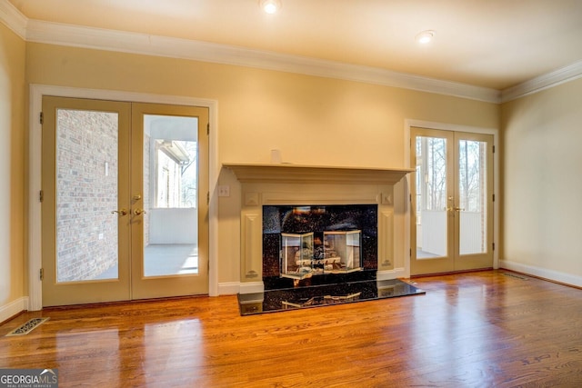 unfurnished living room featuring crown molding, hardwood / wood-style flooring, a high end fireplace, and french doors