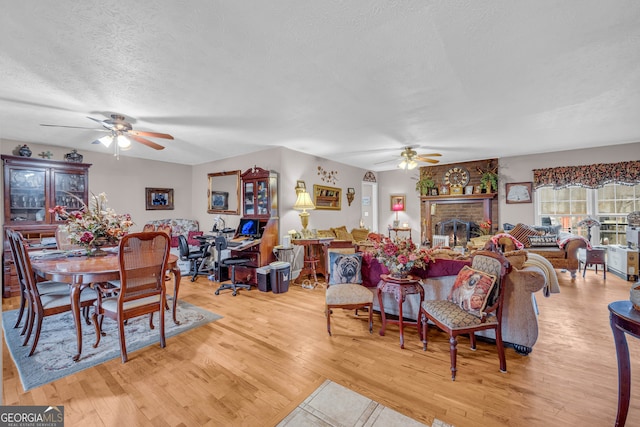 dining space featuring a brick fireplace, light hardwood / wood-style flooring, a textured ceiling, and ceiling fan