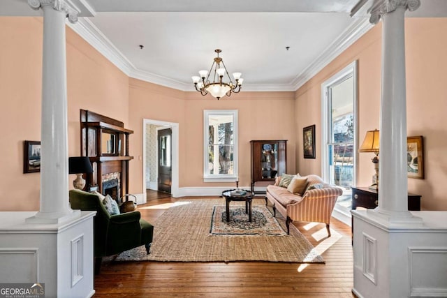 living area featuring an inviting chandelier, wood-type flooring, ornamental molding, and ornate columns