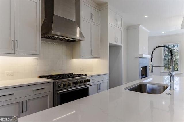 kitchen with high end stainless steel range oven, light stone countertops, sink, and wall chimney exhaust hood