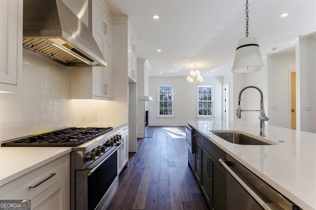 kitchen featuring appliances with stainless steel finishes, decorative light fixtures, white cabinetry, sink, and wall chimney range hood