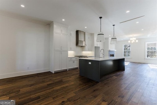 kitchen featuring sink, dark hardwood / wood-style flooring, pendant lighting, a kitchen island with sink, and wall chimney range hood