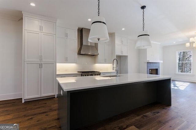 kitchen featuring pendant lighting, an island with sink, sink, dark hardwood / wood-style flooring, and wall chimney range hood