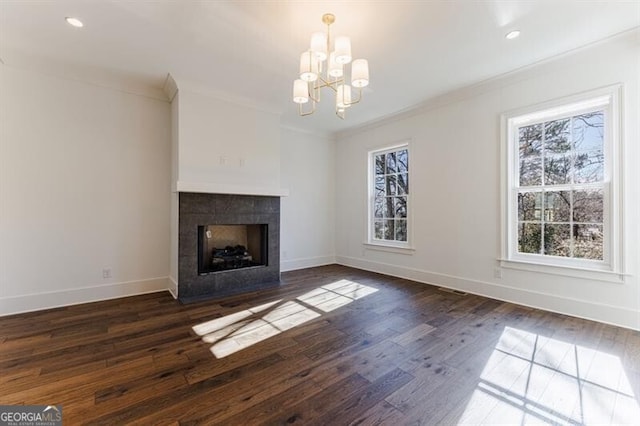 unfurnished living room with crown molding, an inviting chandelier, a tiled fireplace, and dark wood-type flooring