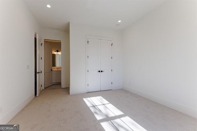 unfurnished bedroom with light colored carpet, a closet, and ensuite bathroom