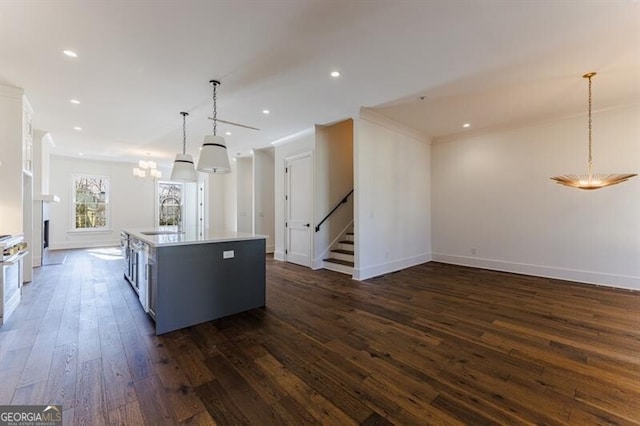 kitchen with sink, crown molding, dark wood-type flooring, a center island with sink, and decorative light fixtures