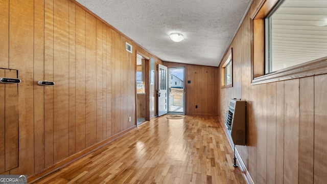 corridor with wood walls, light hardwood / wood-style floors, heating unit, and a textured ceiling