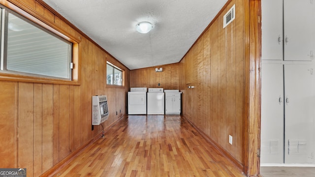 hallway featuring washer and dryer, heating unit, wood walls, a textured ceiling, and light hardwood / wood-style flooring