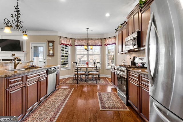 kitchen featuring appliances with stainless steel finishes, decorative light fixtures, sink, dark stone counters, and dark wood-type flooring