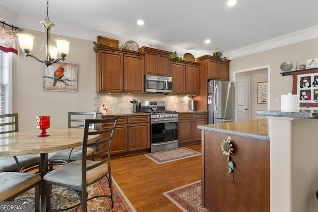 kitchen featuring hanging light fixtures, light hardwood / wood-style flooring, appliances with stainless steel finishes, light stone countertops, and backsplash