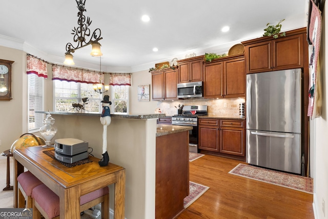 kitchen with hanging light fixtures, crown molding, stainless steel appliances, and a kitchen bar