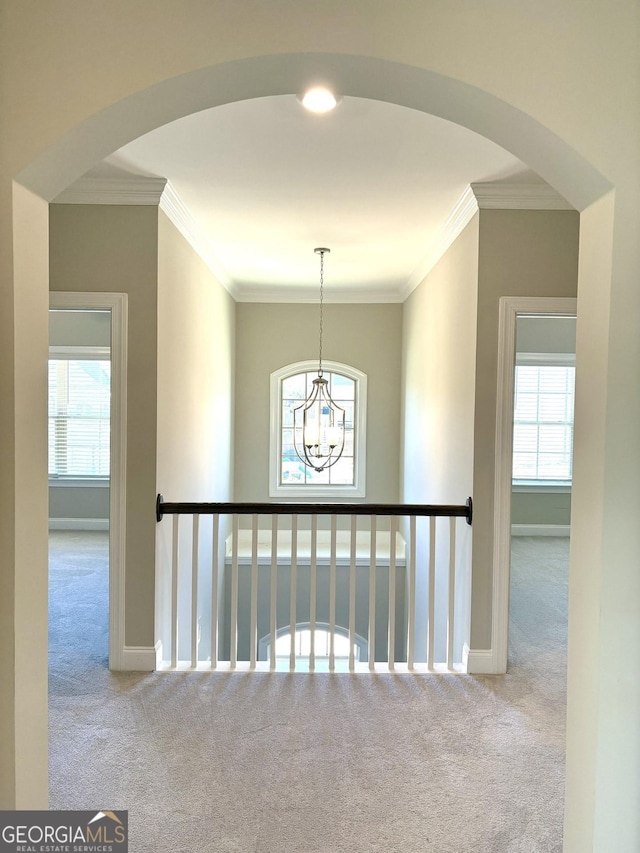 hallway featuring crown molding, light carpet, and an inviting chandelier